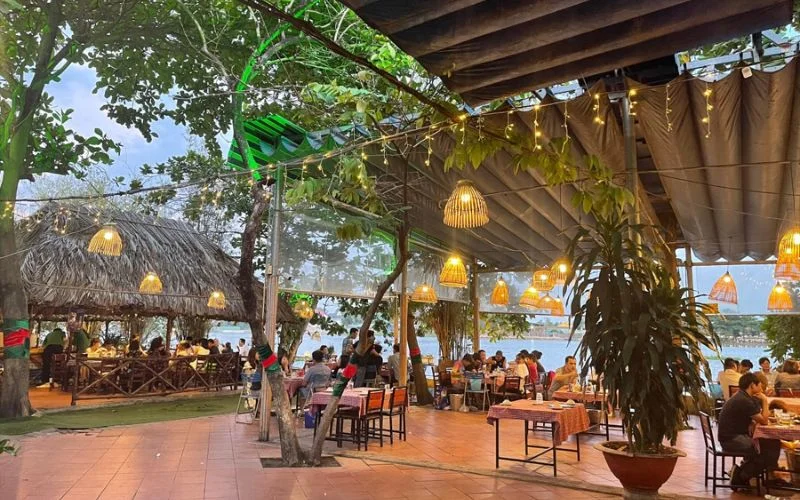 Không gian sân vườn ven sông với ánh đèn ấm áp, thích hợp cho những buổi gặp gỡ và dùng bữa buổi tối