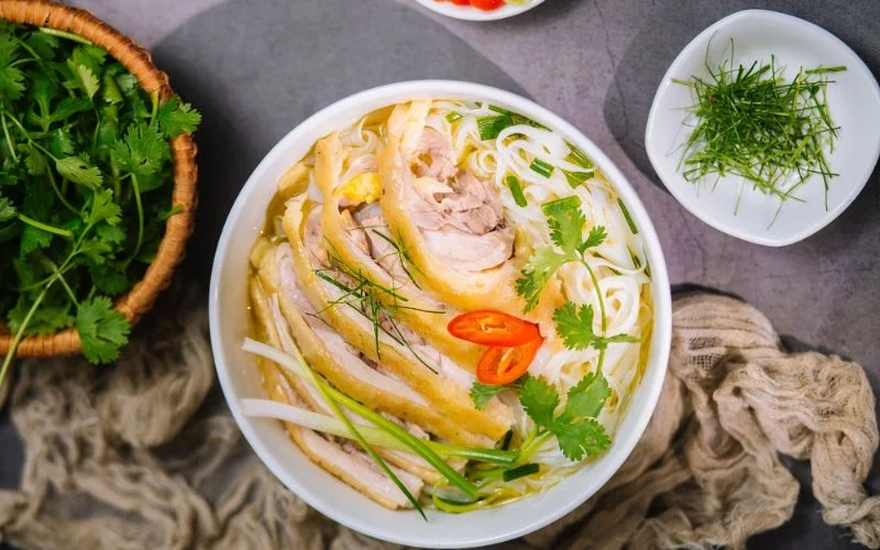 Hoàn thiện tô phở gà với bánh phở, thịt gà và rau thơm